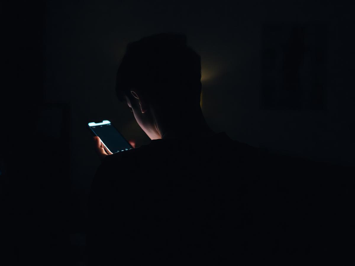 Silhouette of person in dim room looking at phone with back discomfort